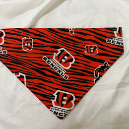 A triangular pet bandana featuring a red and black tiger stripe pattern with Cincinnati Bengals logos, displayed on a white fabric background.