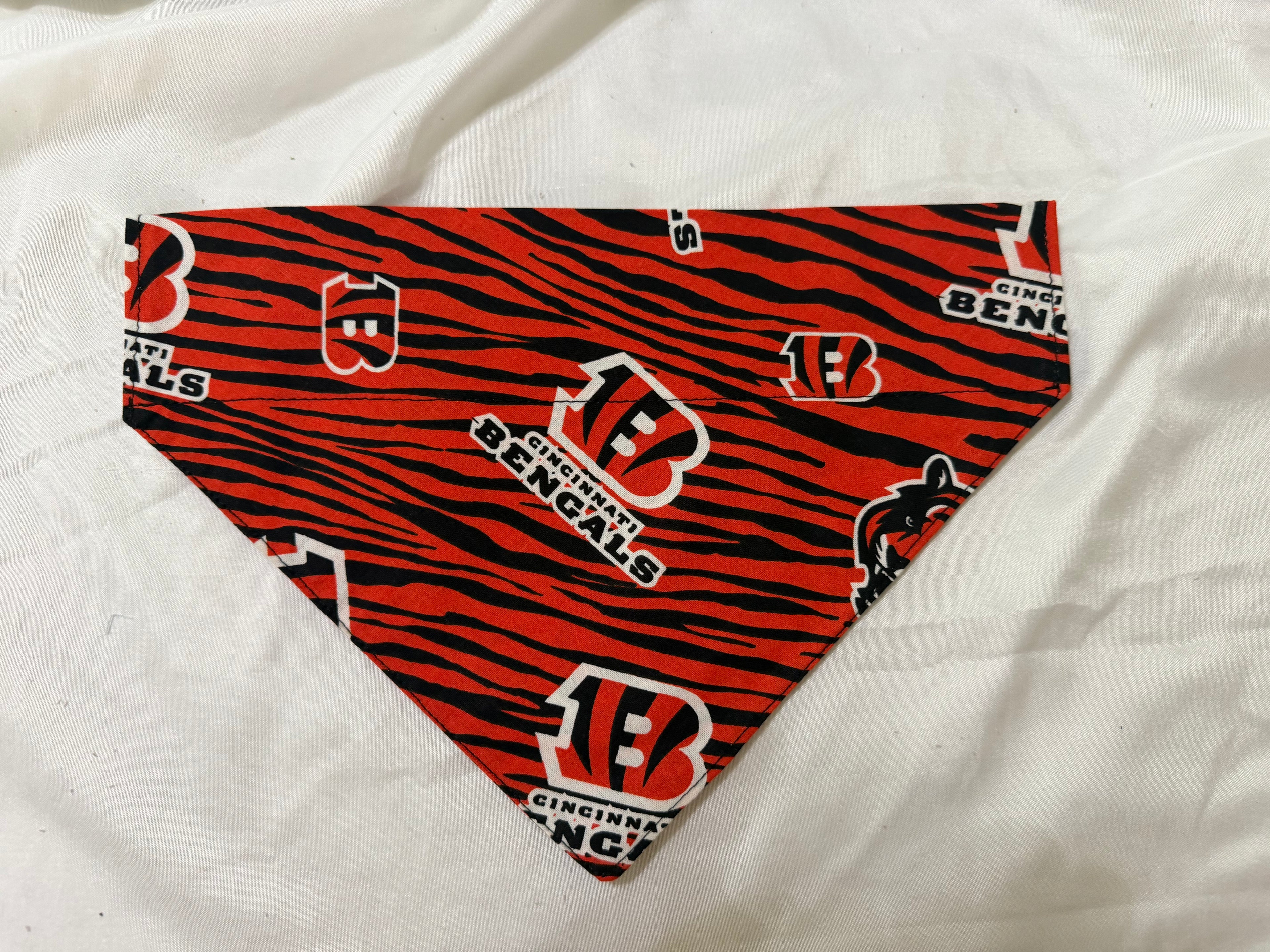 A triangular pet bandana featuring a red and black tiger stripe pattern with Cincinnati Bengals logos, displayed on a white fabric background.